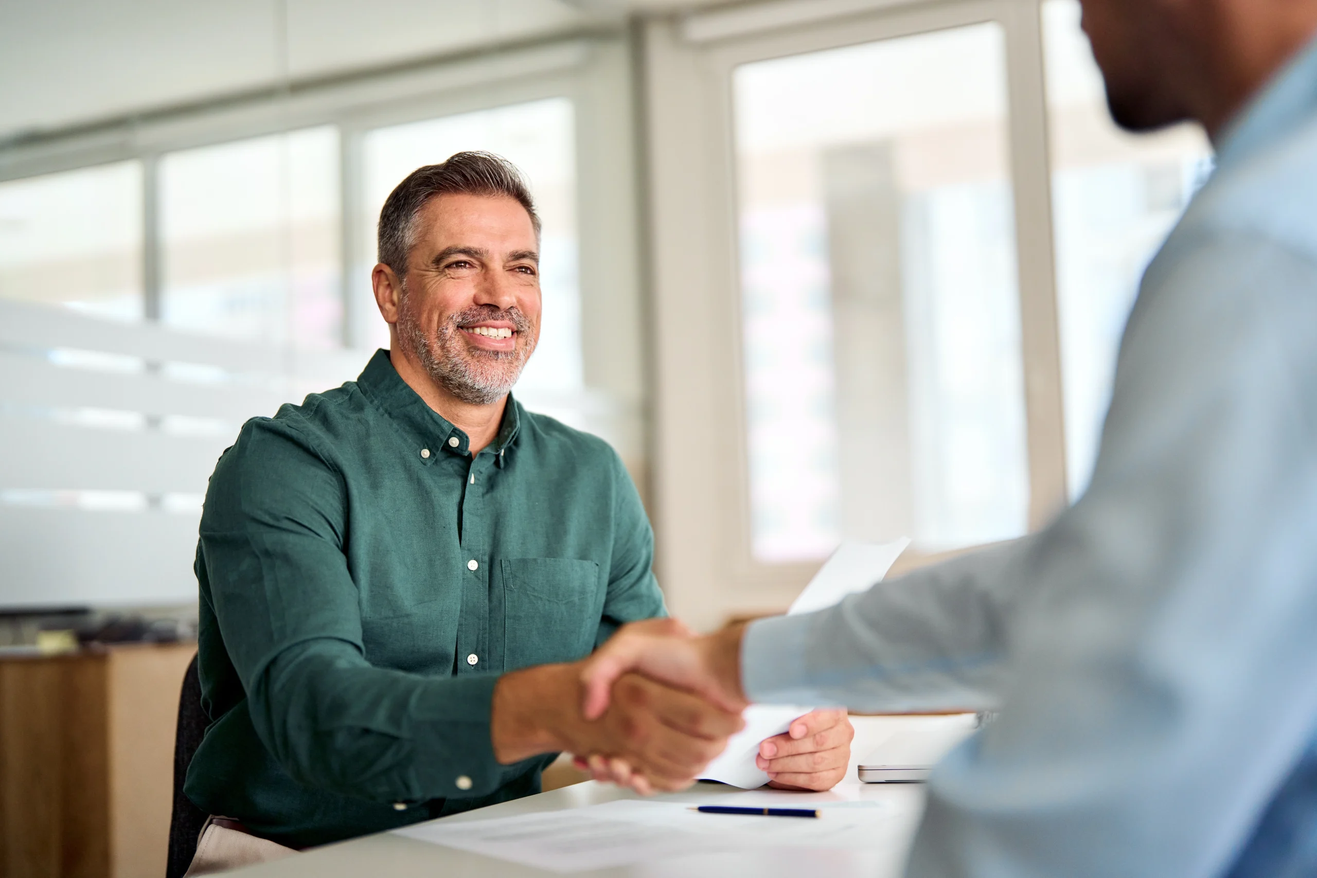 Two men discussing accounting while shaking hands and smiling at a table