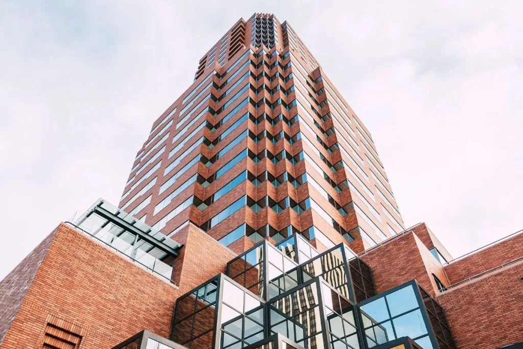 A tall, modern building rises against a cloudy sky, showcasing glass and brick architecture