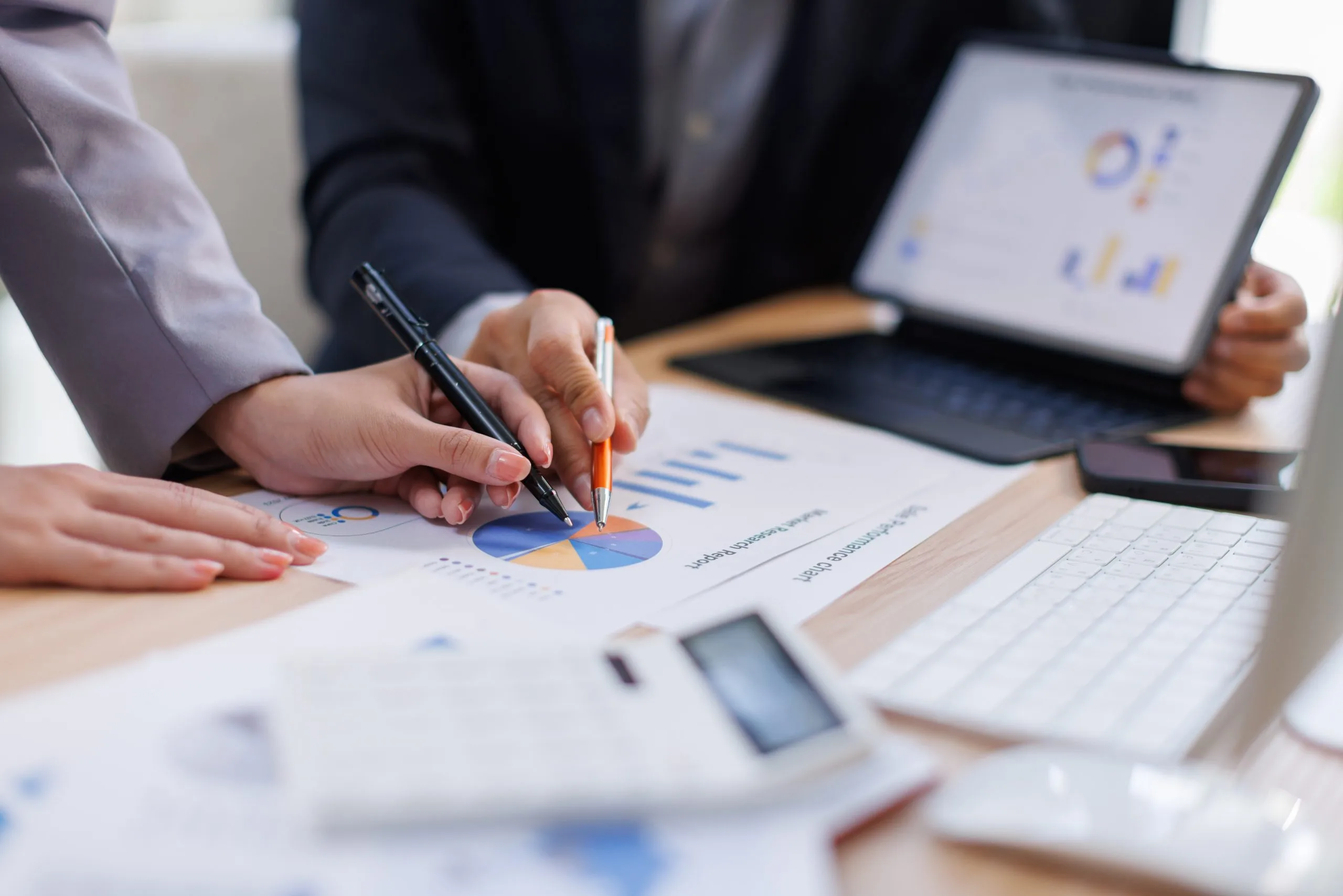 Hands are shown analyzing charts and graphs on paper and a laptop